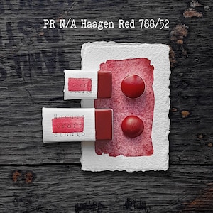 Könnte beinhalten: Zwei rechteckige Aquarellnäpfchen und zwei kreisförmige Aquarelltropfen in Haagen Red 788/52. Die Näpfchen sind in weiße Papieretiketten mit dem schwarzen Text Nordic Craft Studio eingewickelt. Ein roter Farbauftrag befindet sich auf strukturiertem weißem Papier.
