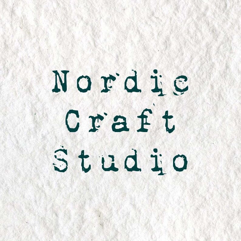 Puede incluir: Un fondo de papel blanco texturizado con el texto verde oscuro Nordic Craft Studio impreso en una fuente estilo m&aacute;quina de escribir. Las letras tienen un aspecto desgastado y estampado, creando un alto contraste sobre la superficie rugosa.
