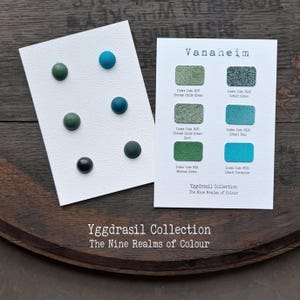 Könnte beinhalten: Zwei weiße Karten aus der Yggdrasil Collection The Nine Realms of Colour. Eine Karte zeigt sechs kreisförmige Knöpfe in Grün- und Blautönen. Die andere Karte zeigt sechs rechteckige Farbmuster mit Beschriftungen wie Chrome Oxide Green, Cobalt Green, Chrome Oxide Green Dark, Cobalt Teal, Nitroso Green und Cobalt Turquoise.
