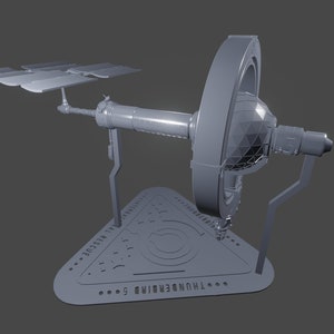 Puede incluir: Un modelo gris de una estación espacial impreso en 3D con paneles solares y una sección rotatoria. El modelo está sobre una base triangular con un diseño.