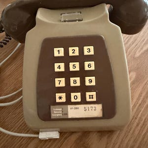 May include: A vintage beige and brown push-button telephone. The phone has a rectangular base with a brown keypad featuring white number buttons. The handset is brown. The phone has a label with the number 5173.