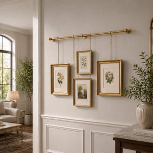 May include: A gold-toned metal wall rod with four hanging picture frames suspended by thin chains. The frames are arranged in a staggered layout, each containing botanical or landscape art prints with off-white matting and gold-toned borders.