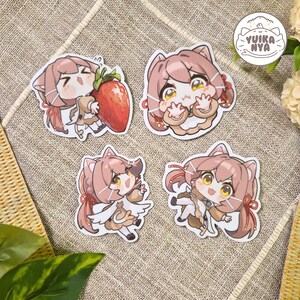 May include: Four anime-style stickers showing a character with cat ears and brown hair. The stickers show the character in different poses, including holding a strawberry. The stickers have a white border and are on a textured surface.