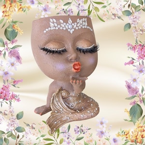 May include: A brown mermaid-shaped planter with a textured finish, featuring a rhinestone tiara on the forehead, long black eyelashes, and a metallic orange mouth. The mermaid tail is decorated with scattered clear rhinestones throughout the surface.