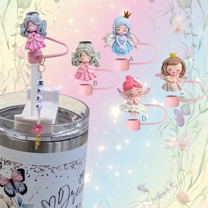 May include: A collection of decorative straw toppers featuring angel figurines in various colors. One topper is attached to a tumbler with the name "MARY" spelled out on a charm. The toppers have pink, blue, and white accents.