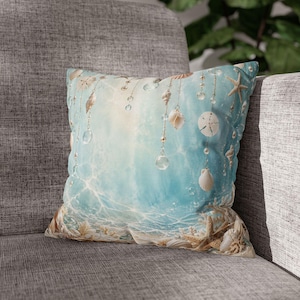 May include: A square throw pillow featuring a light blue aquatic background with a pattern of hanging seashells, starfish, and clear glass beads. The bottom edge displays a collection of various seashells and starfish resting on a sandy base.