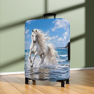Peut inclure: Une valise à roulettes arborant une impression haute résolution d'un cheval blanc à la longue crinière fluide galopant dans les vagues de l'océan sous un ciel bleu vif parsemé de nuages blancs. La valise possède une poignée et quatre roues.