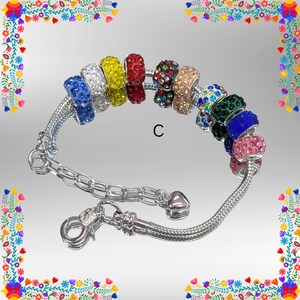 May include: A silver charm bracelet with a variety of colorful, rhinestone-studded beads. The beads are in shades of blue, white, yellow, red, black, tan, green, and pink. The bracelet has a lobster clasp closure.