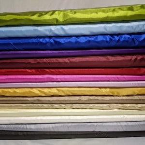 Può includere: Una pila di 12 tessuti di raso di diversi colori. I colori sono verde, azzurro, blu, viola, bordeaux, rosa, oro, beige, crema, bianco, grigio e nero.