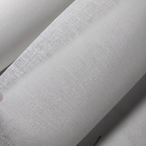 May include: Close-up of a roll of white fabric. The fabric has a fine, open weave, and a slightly textured surface. The fabric is tightly rolled, with the edges visible. The color is a bright, clean white.