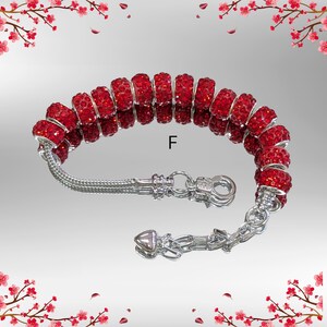 May include: A red beaded bracelet with a silver chain and clasp. The bracelet features multiple round, red beads with a sparkling texture. The clasp and chain are made of silver-colored metal. The letter "F" is visible on the background.