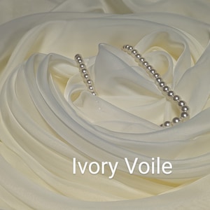 May include: Ivory voile fabric with a strand of white pearls draped on top. The fabric is gathered and folded to create a soft, flowing look.  Ivory Voile.