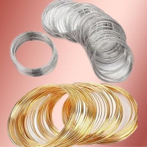 May include: An assortment of silver and gold-colored wire rings. The silver rings are stacked in two groups, with one smaller ring separate. The gold rings are stacked in a larger group. The background is a gradient of pink and red.
