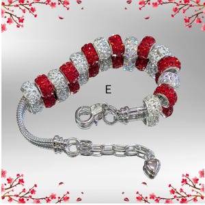 May include: Silver charm bracelet with red and clear crystal beads. The bracelet has a lobster clasp and a heart-shaped charm. The beads are round and faceted, reflecting light. The bracelet is on a light gray background.