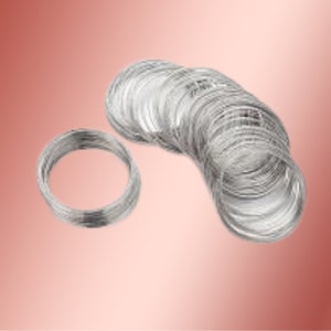 May include: A collection of multiple silver-colored metal wire coils arranged in a cluster. Each coil consists of several circular loops of thin, flexible wire, creating a stack of metallic rings that appear uniform in size and texture.