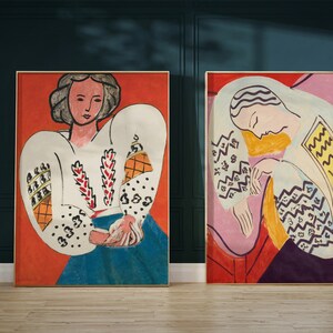 May include: Two framed paintings of women in a cubist style. The painting on the left features a woman with short, dark hair wearing a white blouse with a geometric pattern. The painting on the right features a woman with long, dark hair wearing a white blouse with a geometric pattern.