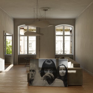 May include: A black and white photograph of three women, framed and hanging on a wall in a living room. The women are looking at the camera with serious expressions. The room is decorated in a minimalist style with white walls and a large window.