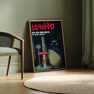 May include: A framed poster featuring Japanese text and a cartoon illustration of a girl with an umbrella and a large, round creature. A wooden chair with a woven back and a round, woven rug are also in the image.