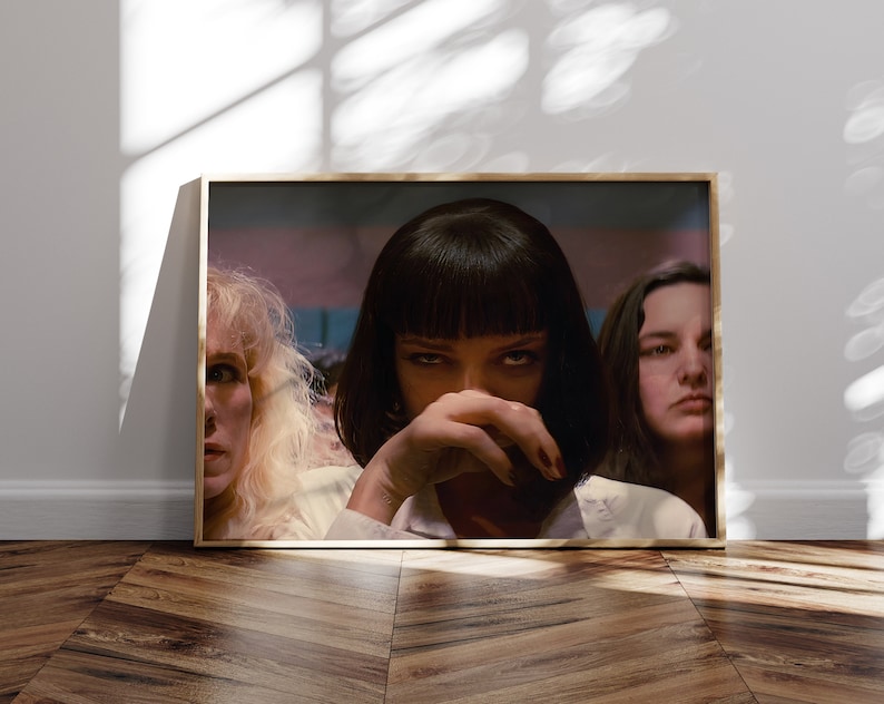 May include: A close-up shot of three women, the woman in the center has dark hair and is looking directly at the camera with a serious expression. The woman on the left has blonde hair and is looking to the right. The woman on the right has dark hair and is looking to the left. The women are all wearing white shirts.