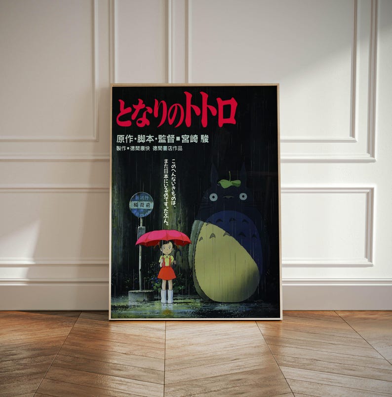 May include: A framed poster featuring the Japanese animated film "My Neighbor Totoro." The poster shows a young girl with a red umbrella standing in the rain, with Totoro and a bus stop in the background. Japanese text is visible at the top.