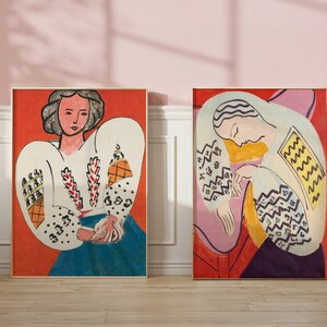May include: Two framed paintings of women with colorful patterns on their clothing. The woman on the left is wearing a white blouse with red and yellow patterns. The woman on the right is wearing a white blouse with yellow and blue patterns. Both paintings have a red background.