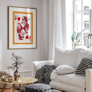May include: A framed print of a Queen of Hearts playing card with a woman wearing sunglasses and holding a glass of wine. The card is set against a yellow background with a red heart in the corner.