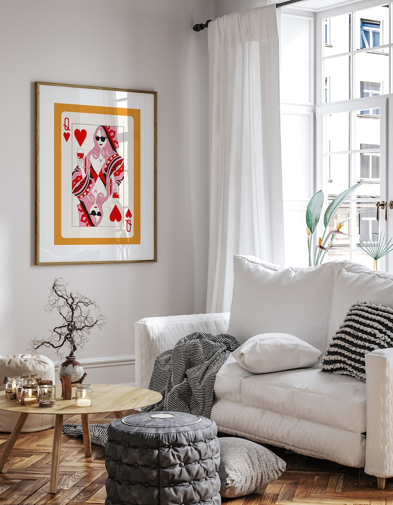 May include: A framed print of a Queen of Hearts playing card with a woman wearing sunglasses and holding a glass of wine. The card is set against a yellow background with a red heart in the corner.