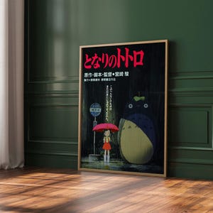May include: A framed poster featuring Japanese text and an illustration from the animated film "My Neighbor Totoro." The artwork depicts a young girl with a red umbrella, Totoro, and a bus stop in a rainy scene.