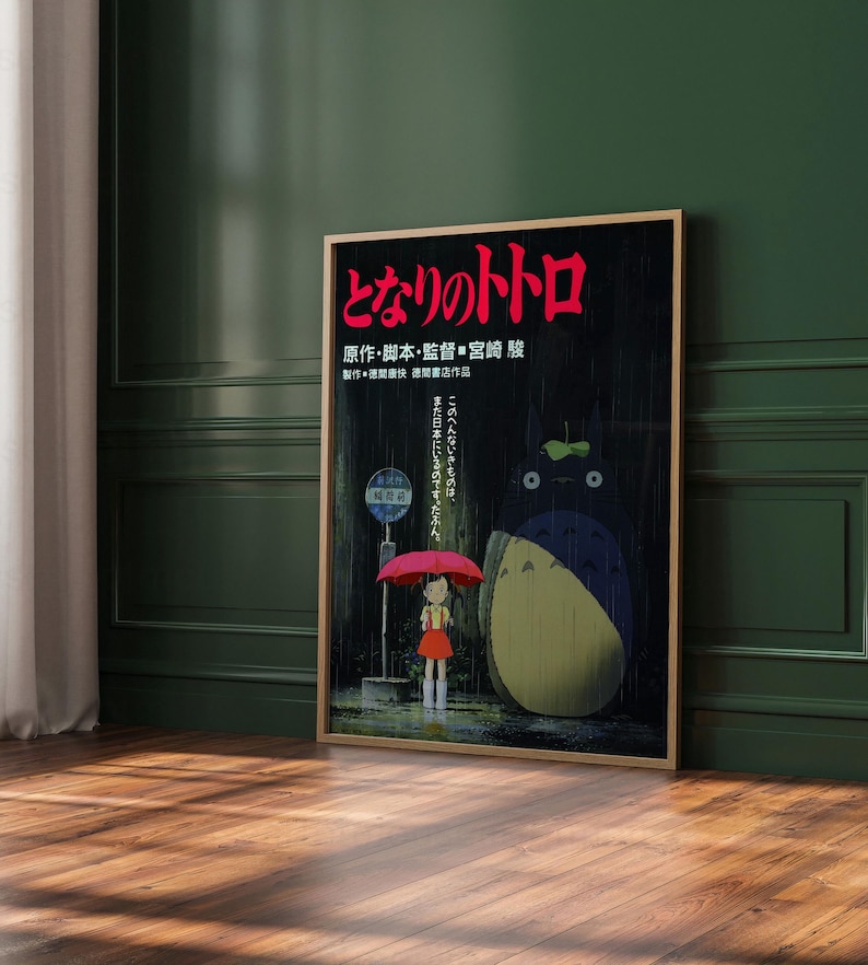 May include: A framed poster featuring Japanese text and an illustration from the animated film "My Neighbor Totoro." The artwork depicts a young girl with a red umbrella, Totoro, and a bus stop in a rainy scene.