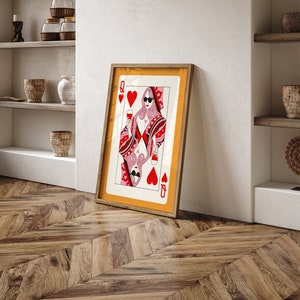May include: A framed print of the Queen of Hearts playing card. The queen is wearing sunglasses and holding a glass of wine. The card is set against a yellow background.