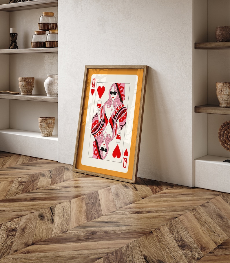 May include: A framed print of the Queen of Hearts playing card. The queen is wearing sunglasses and holding a glass of wine. The card is set against a yellow background.