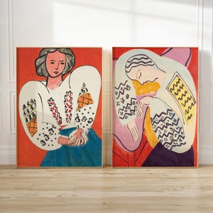 May include: Two framed paintings of women in white blouses with colorful geometric patterns. The paintings are set against a red background.