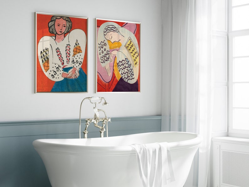 May include: Two framed paintings of women in colorful clothing. The paintings are hanging on a white wall above a white bathtub.