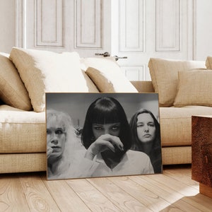 May include: Black and white photograph of three women. The woman in the center has short black hair and is looking at the camera. The woman on the left has blonde hair and is looking to the right. The woman on the right has brown hair and is looking to the left.