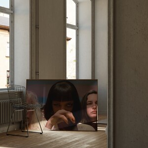 May include: A framed poster featuring a close-up of a woman with dark hair and a serious expression. She is wearing a black shirt and has her hand covering her mouth. A second woman with long dark hair is visible in the background.