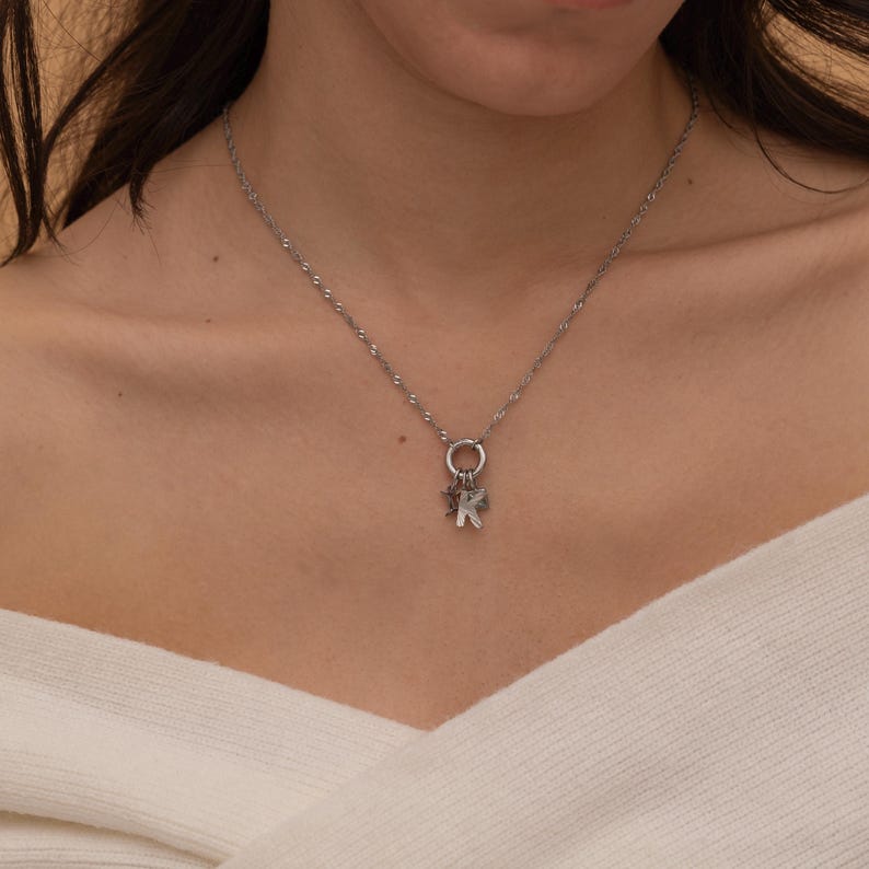 May include: A silver chain necklace with a charm featuring a letter K and a star.