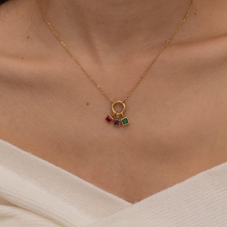 May include: A gold necklace with a circle charm and three dangling square charms with red, purple, and green gemstones.