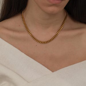 May include: A gold-colored curb chain necklace. The necklace is made of interlocking links and is worn around the neck. The necklace is a simple, yet elegant piece of jewelry.