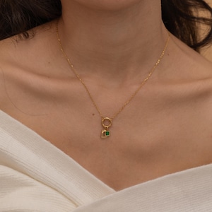 May include: A gold chain necklace with a small green gemstone pendant. The pendant is attached to a gold ring.