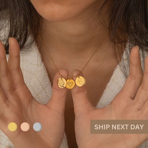 Könnte beinhalten: Goldkette mit drei Anhängern: ein Herz, eine Umrissform des Bundesstaates Kalifornien und eine weitere Umrissform eines Bundesstaates. Die Kette wird von einer Person mit den Händen vor sich getragen.