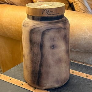 May include: A wooden jar with a lid and a small candle inside. The lid has a leather band with the words "Mom loved forever, always" engraved on it.