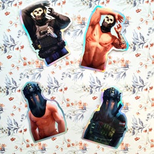 Puede incluir: Cuatro pegatinas holográficas con un personaje con una máscara de calavera. El personaje se representa en diferentes poses, incluyendo una pose táctica con una pistola, una pose sin camisa y una pose con un chaleco táctico.