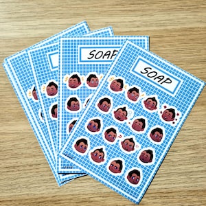 May include: Four blue and white grid-patterned cards with the word "SOAP" in a white rectangle. Each card features a series of cartoon faces with various expressions. The cards are arranged on a light brown wooden surface.