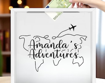 May include: White square shadow box with the text "Amanda's Adventures" in black script, along with a world map outline and a plane. A hand is inserting a 100 Euro bill into the slot at the top.