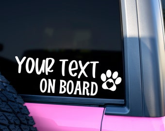 May include: White vinyl decal with the text "YOUR TEXT ON BOARD" and a paw print with a heart in the center. The decal is on the back window of a pink car.