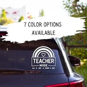 Puede incluir: Una calcomanía blanca con un arcoíris, un corazón y el texto "Teacher Mode" con las palabras "All Day Every Day" debajo. La calcomanía está en la ventana trasera de un coche negro.