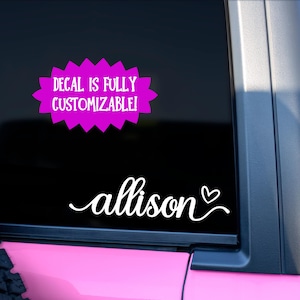 May include: A black car window with a white decal that says "allison" in cursive with a heart symbol. Above the name is a pink starburst shape with the text "DECAL IS FULLY CUSTOMIZABLE!"