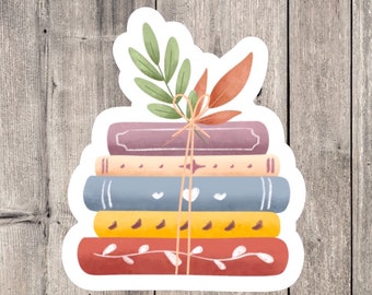 Puede incluir: Una pila de cinco libros atados con cuerda y decorados con una rama de hojas verdes y una hoja roja. Los libros son en tonos de rojo, naranja, amarillo, azul y morado.