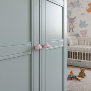 May include: A light blue wardrobe with pink cloud-shaped knobs. The wardrobe is in a nursery with a crib and a colorful mural. A teddy bear and toy blocks are on the floor.
