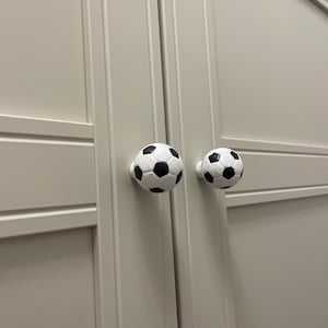 May include: Two white soccer ball shaped cabinet knobs with black stitching.